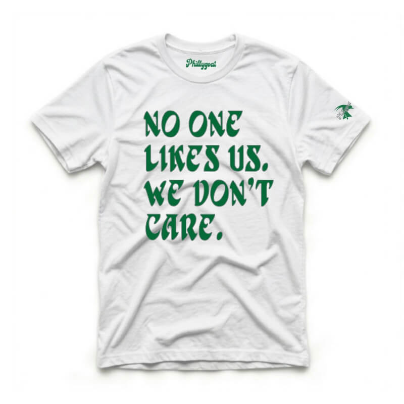 A white short-sleeve t-shirt with the phrase 'NO ONE LIKES US, WE DON'T CARE.' printed in green across the front.