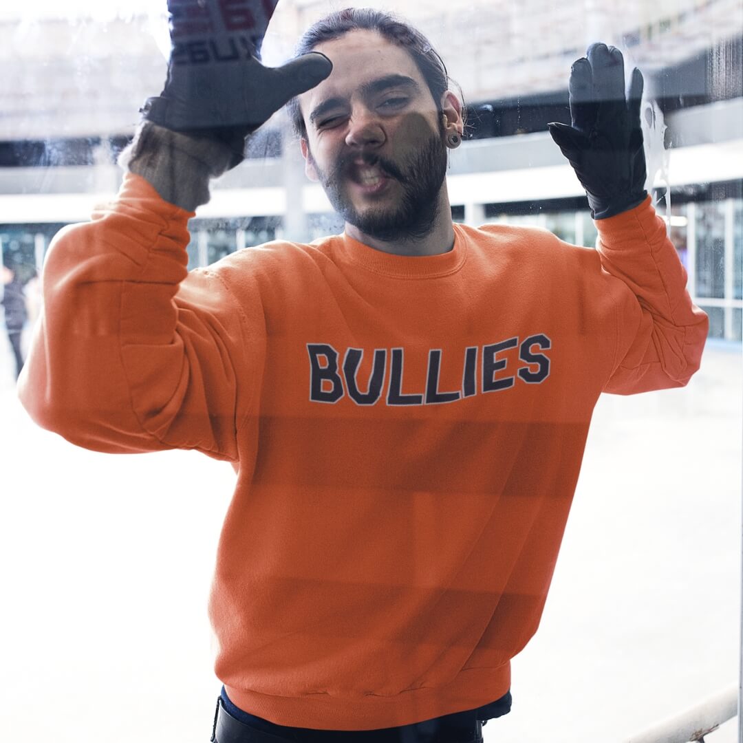 Man wearing a Philadelphia Flyers BULLIES Orange Phillygoat sweatshirt and being cross-check against the boards in a hocket rink