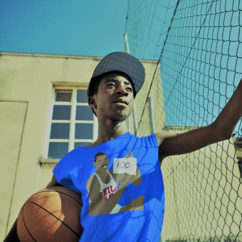 Black teenager wearing a vintage blue Wilt Chamberlain 100 points retro design on a Philadelphia 76ers Phillygoat t-shirt at a North Philly basketball court