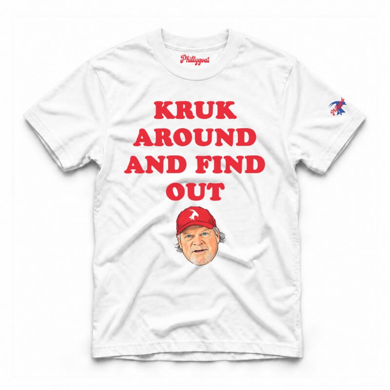 A white short-sleeve graphic t-shirt featuring the text 'KRUK AROUND AND FIND OUT' in cream block letters, a cartoon caricature of John Kruk wearing a blue cap, and a small blue logo on the right sleeve, displayed flat against a white background.